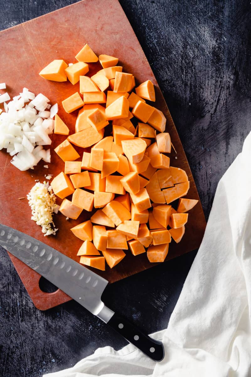 Diced sweet potatoes, onions, and garlic on a cutting board