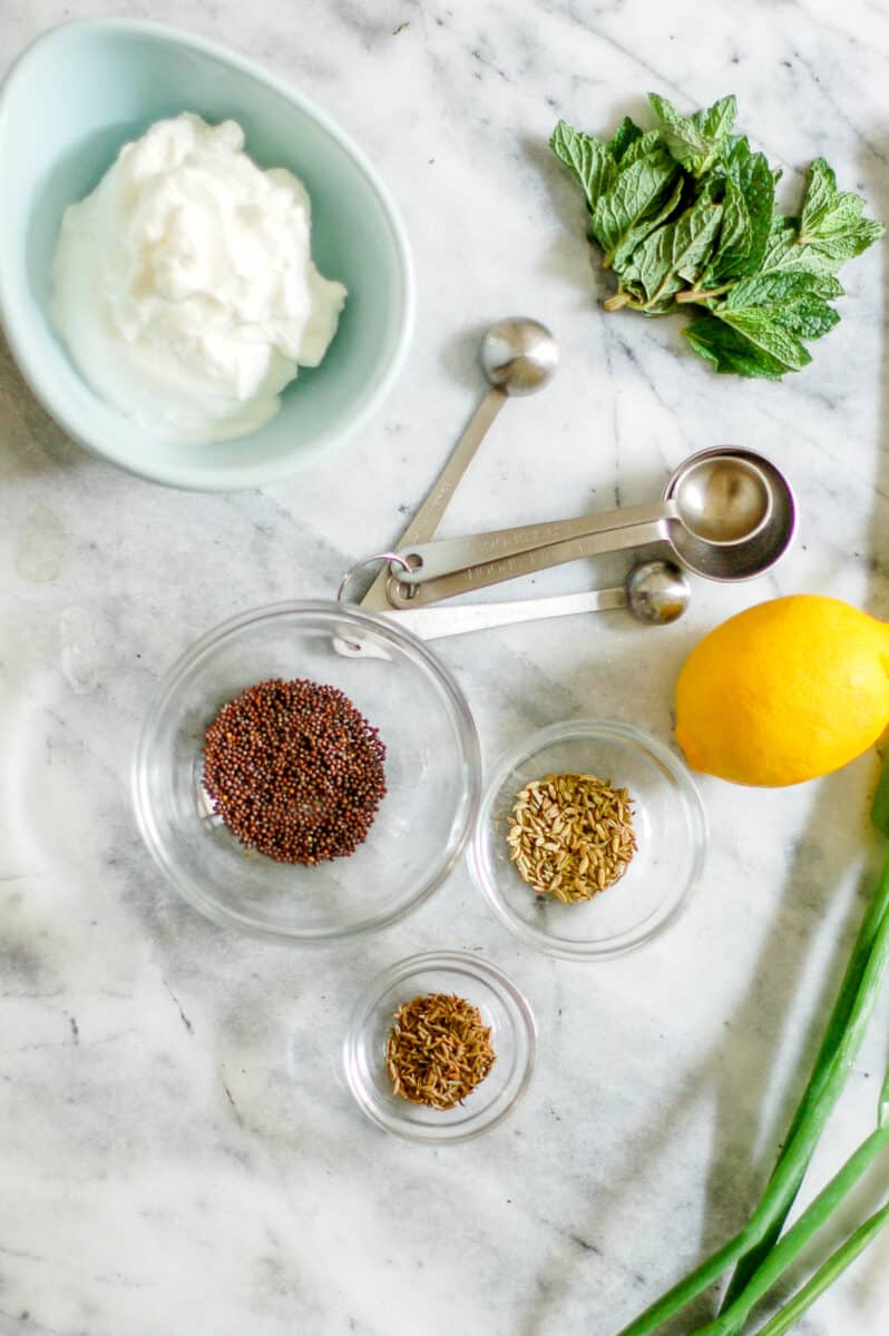 Yogurt, mint, measuring spoons, a lemon and spices in bowls