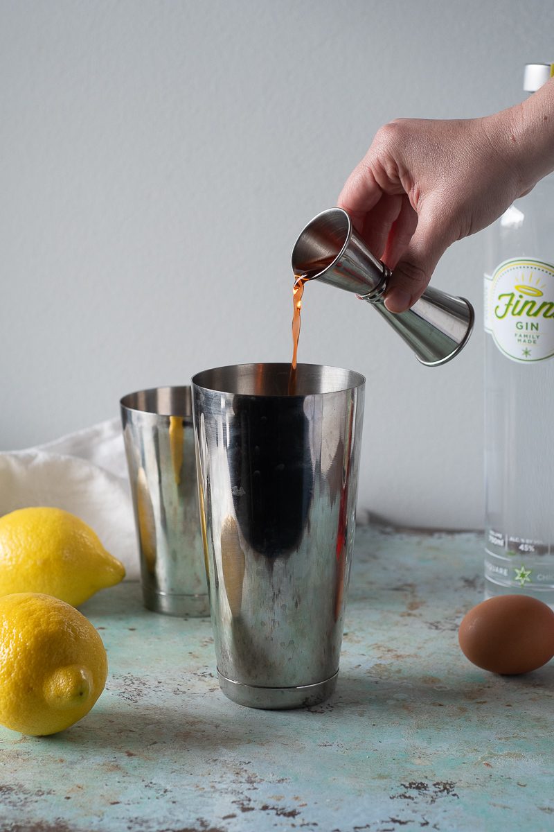 Hand pouring Aperol from jigger into shaker