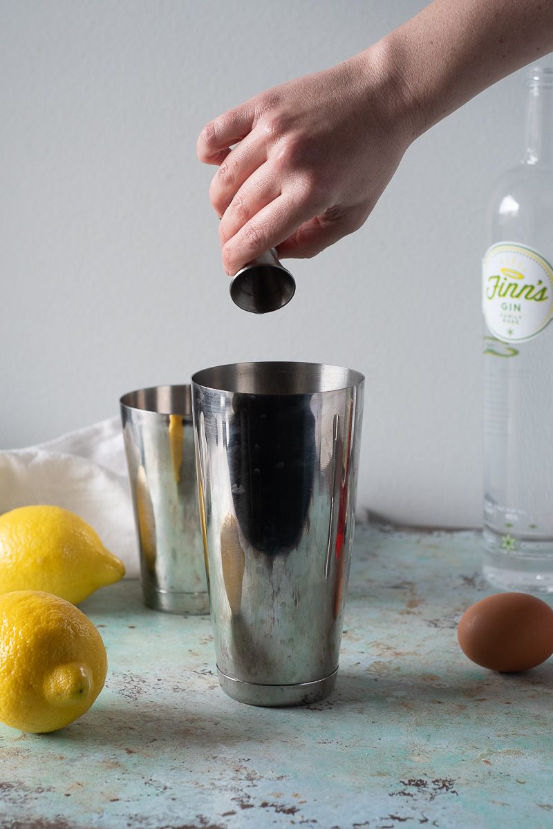 Hand pouring gin from jigger into shaker