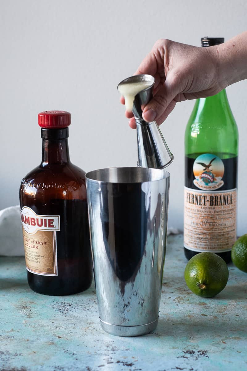 Pouring lime juice from a jigger into a cocktail shaker