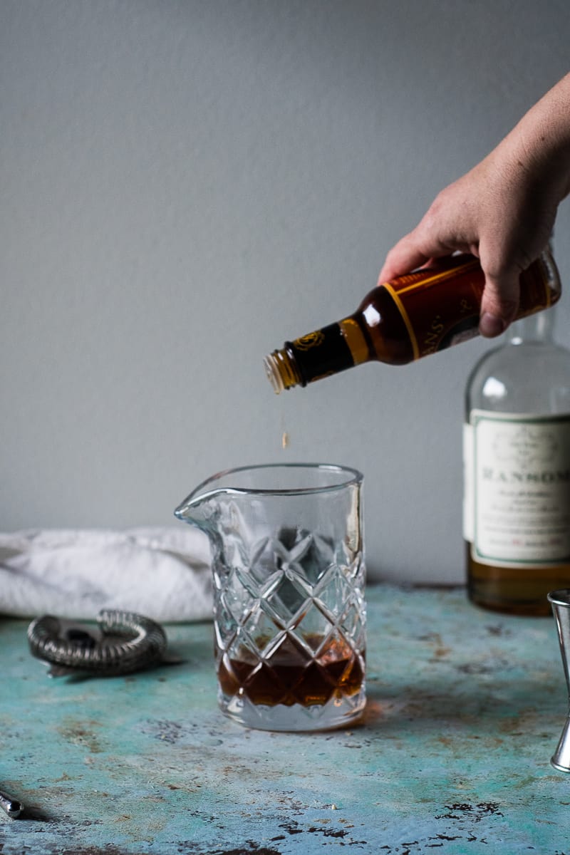 Hand shaking orange bitters into a mixing glass