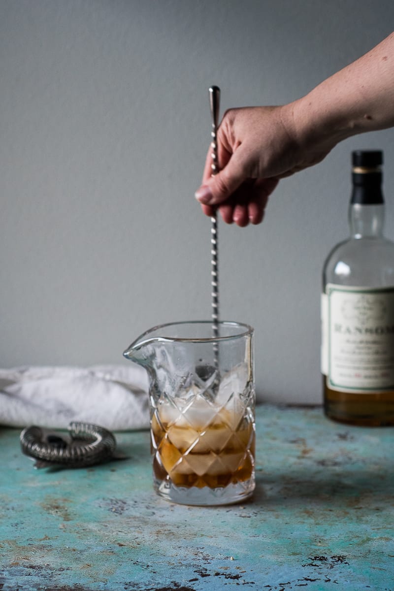 Hand stirring a Martinez cocktail in a cocktail glass with a mixing spoon