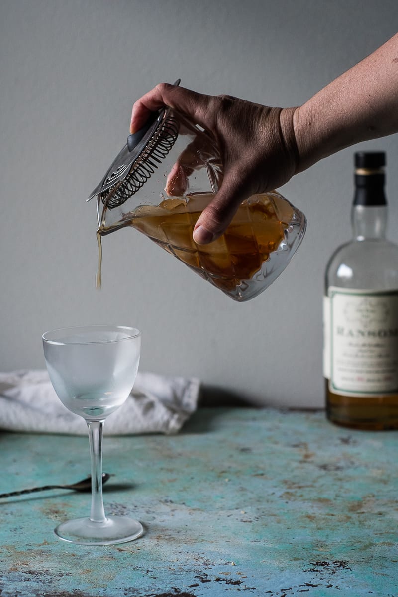 Hand straining Martinez cocktail into a chilled glass