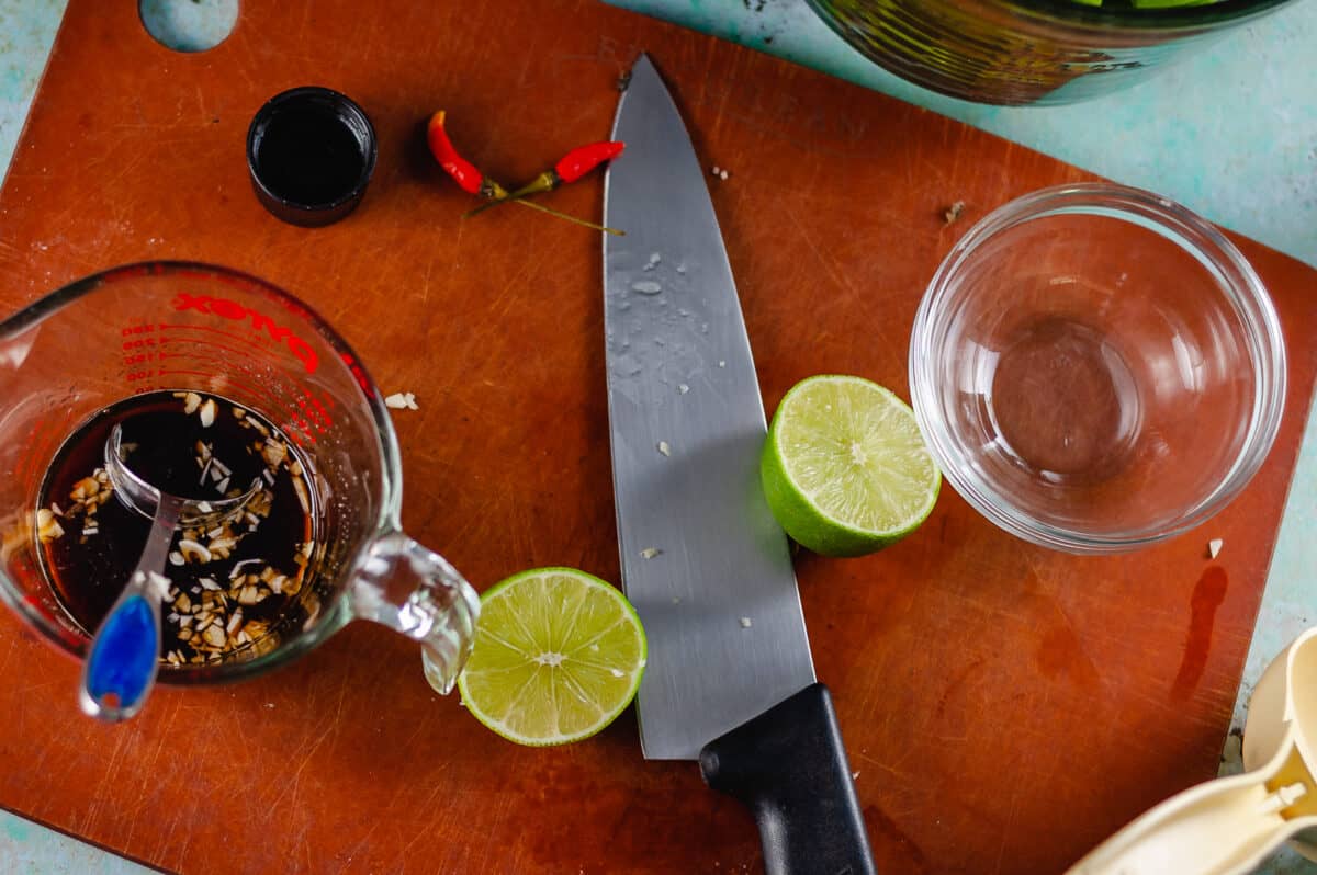 Soy sauce and minced garlic in a glass measuring cup, a lime sliced in half on a cutting board with a chef's knife