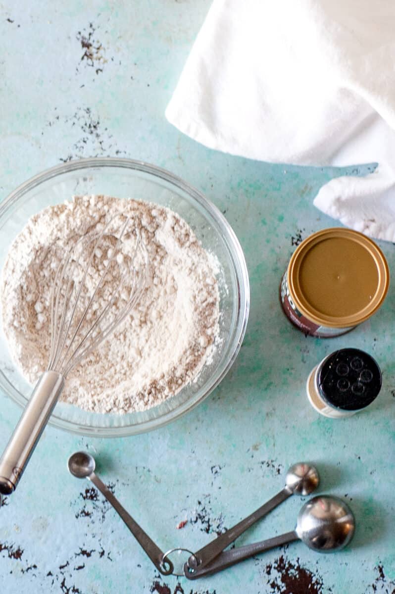 Oat flour in a mixing bowl with baking powder and measuring spoons nearby