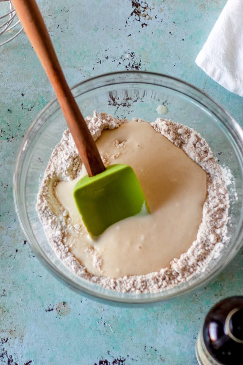 Wet ingredients added to dry ingredients for muffin batter in a glass mixing bowl