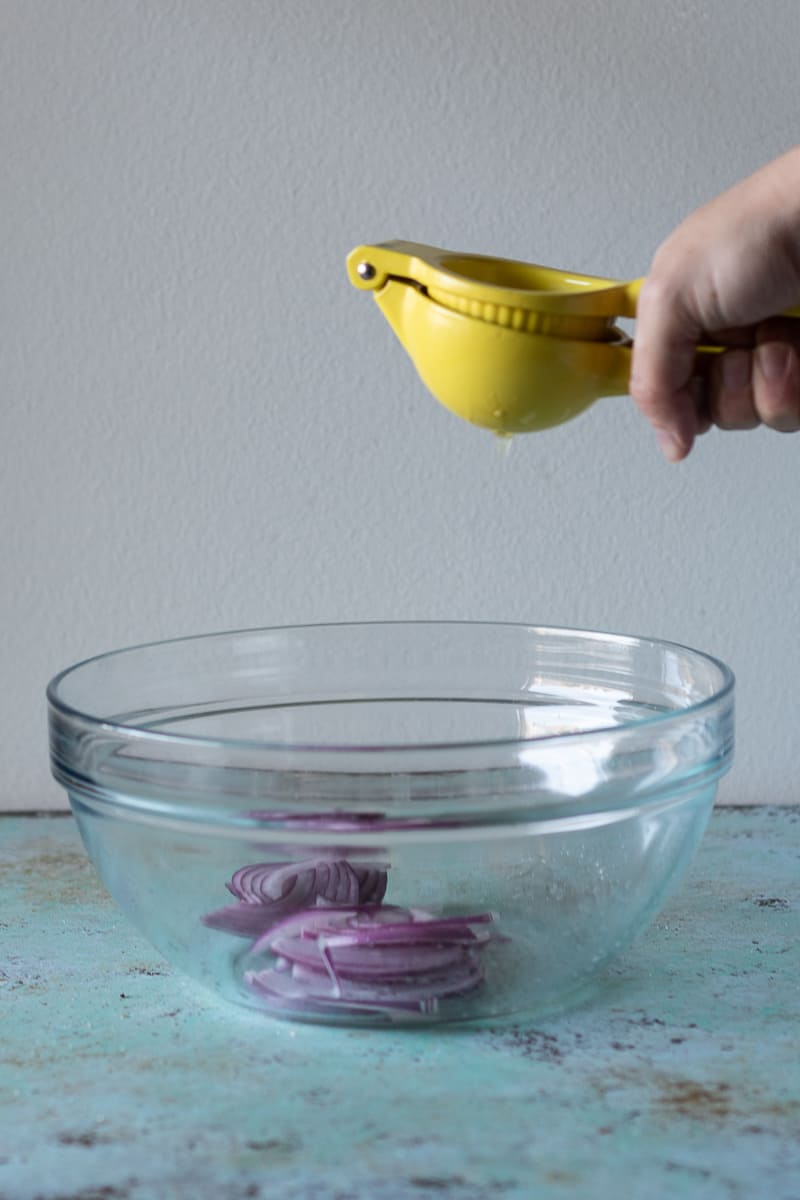 Hand squeezing lime juice into a bowl over thinly sliced red onions