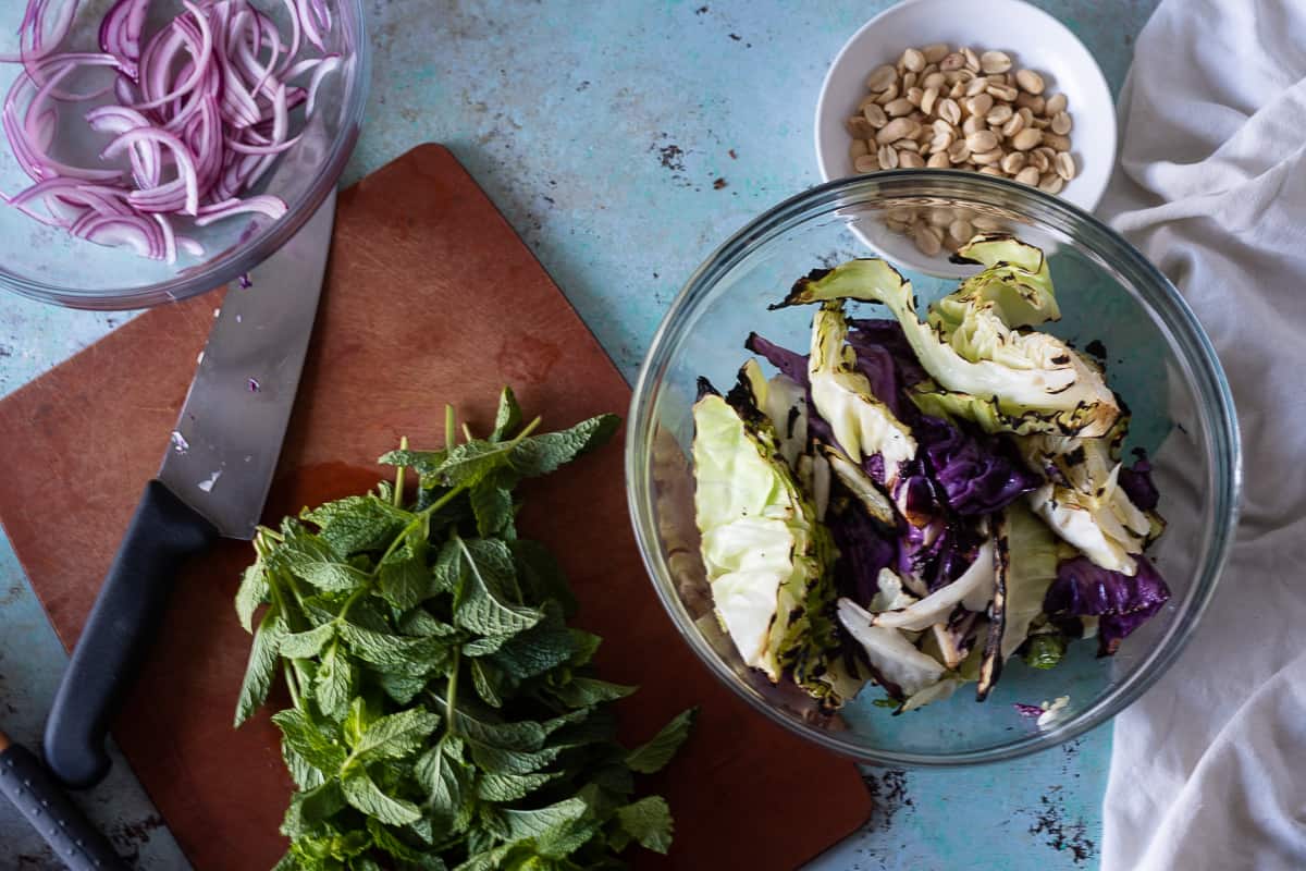 Grilled cabbage wedges in a bowl with peanuts, pickled red onion, and mint around it