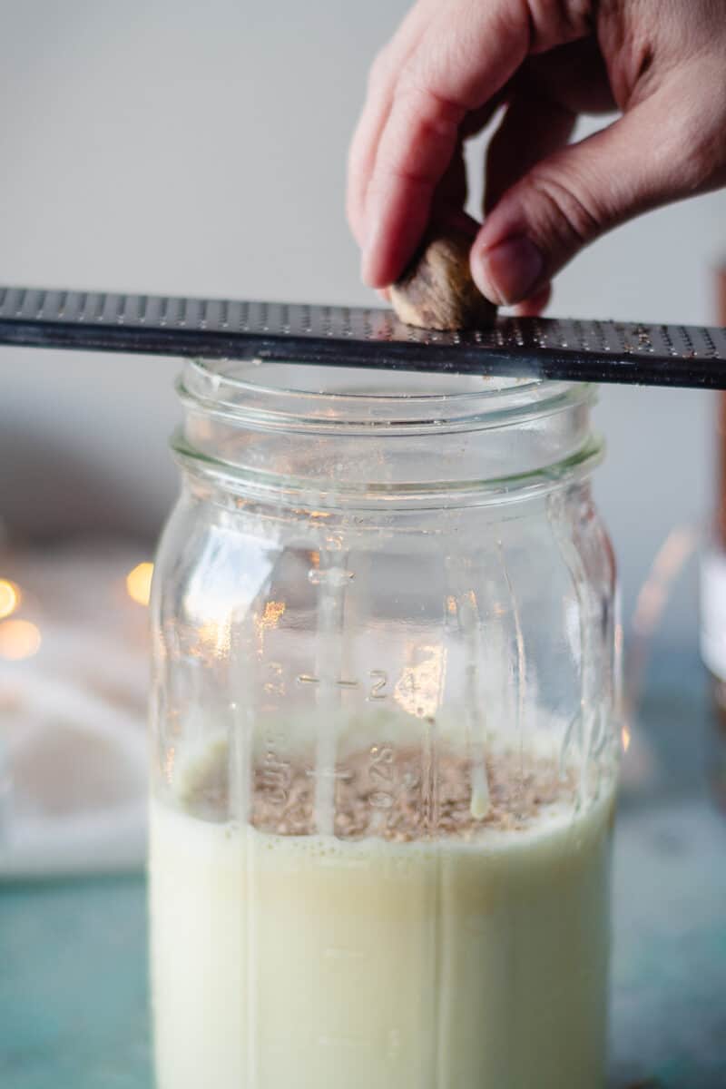 Hand grating nutmeg over a jar of small batch eggnog