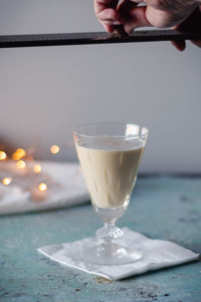 Hand grating nutmeg over a glass of eggnog