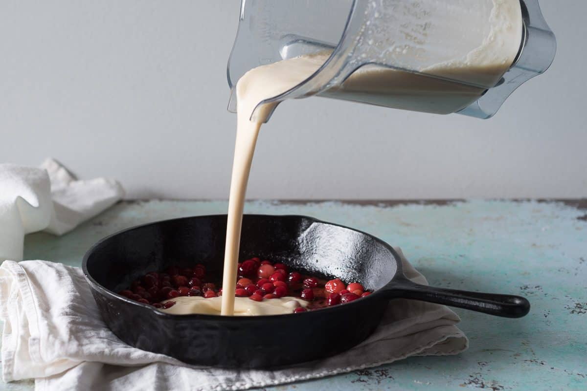 Pouring batter over cranberries in a cast iron skillet