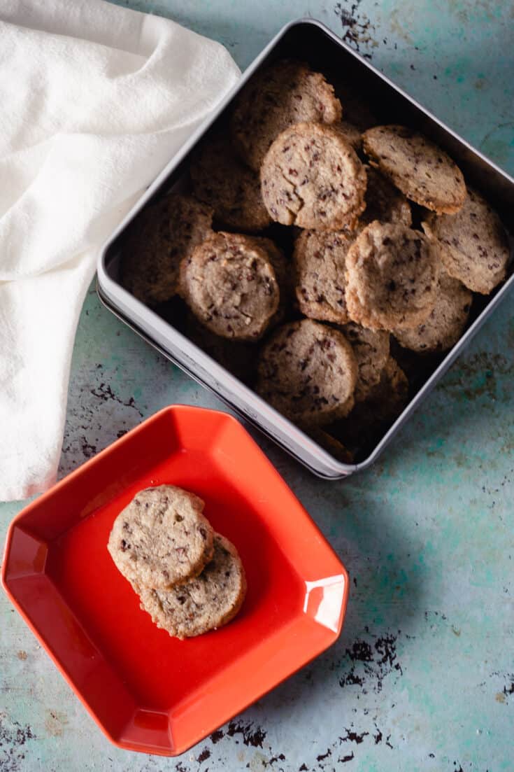 Nibby Buckwheat Cookies on a red plate next to a tin of cookies