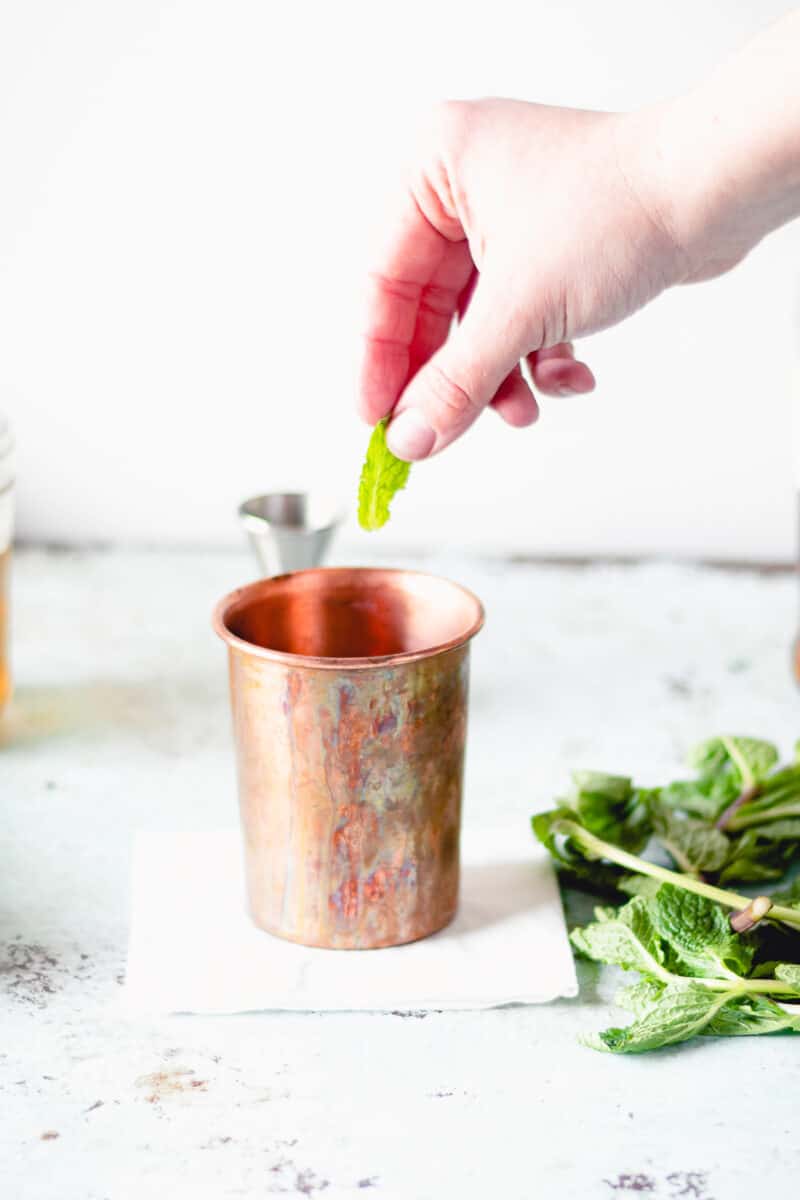 Hand dropping mint into a julep cup