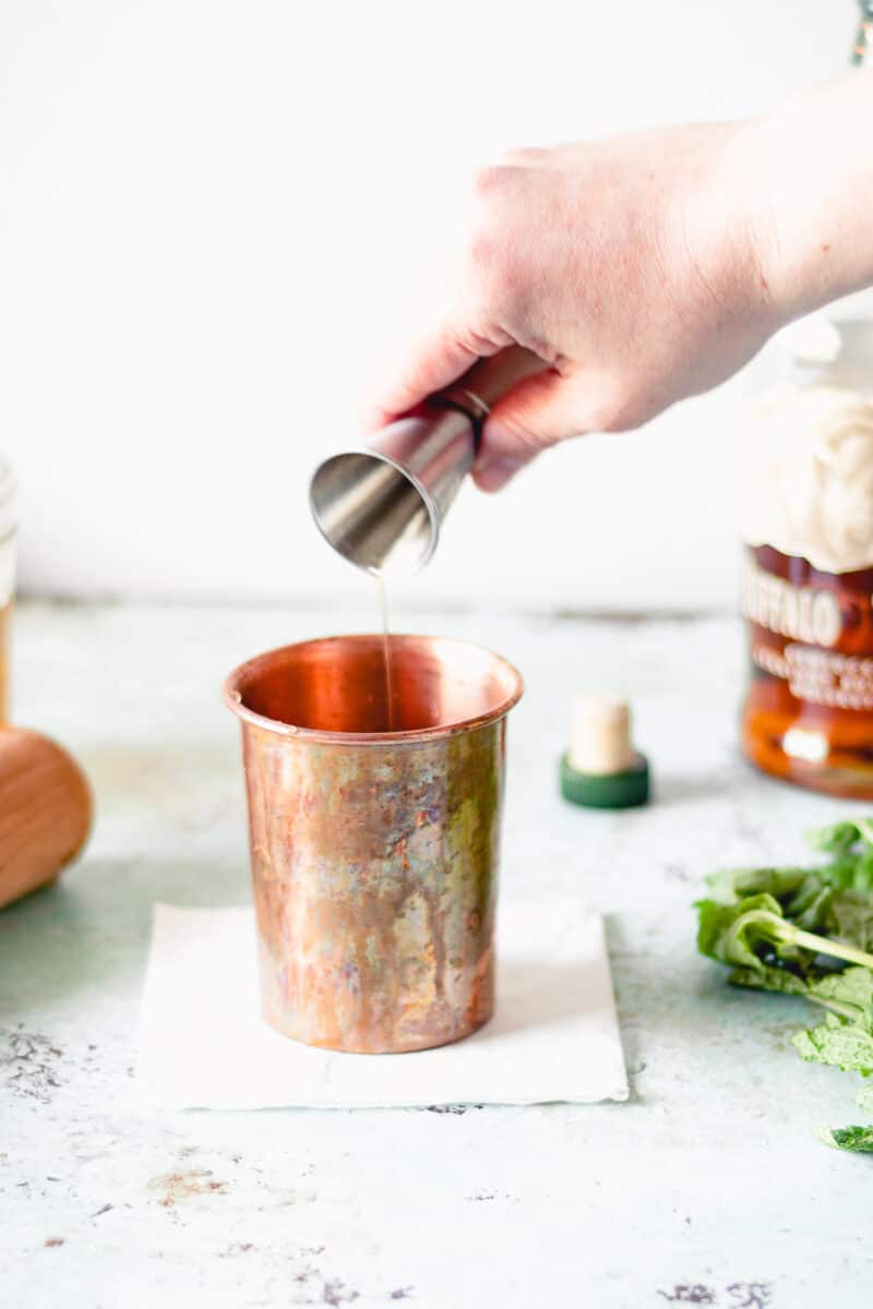 Hand pouring jigger of bourbon into a julep cup