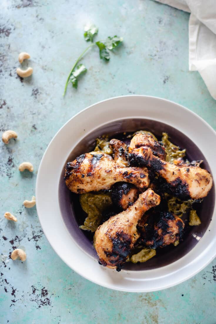 Grilled chicken legs on a plate slathered wtih garlicky cashew sauce