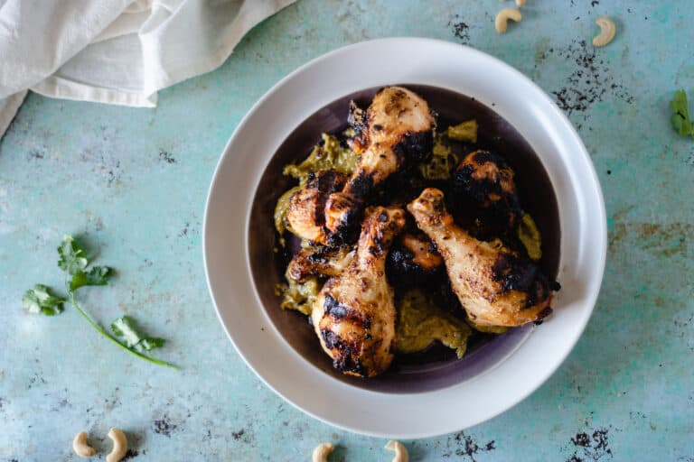 Grilled chicken legs on a plate slathered with garlicky cashew sauce