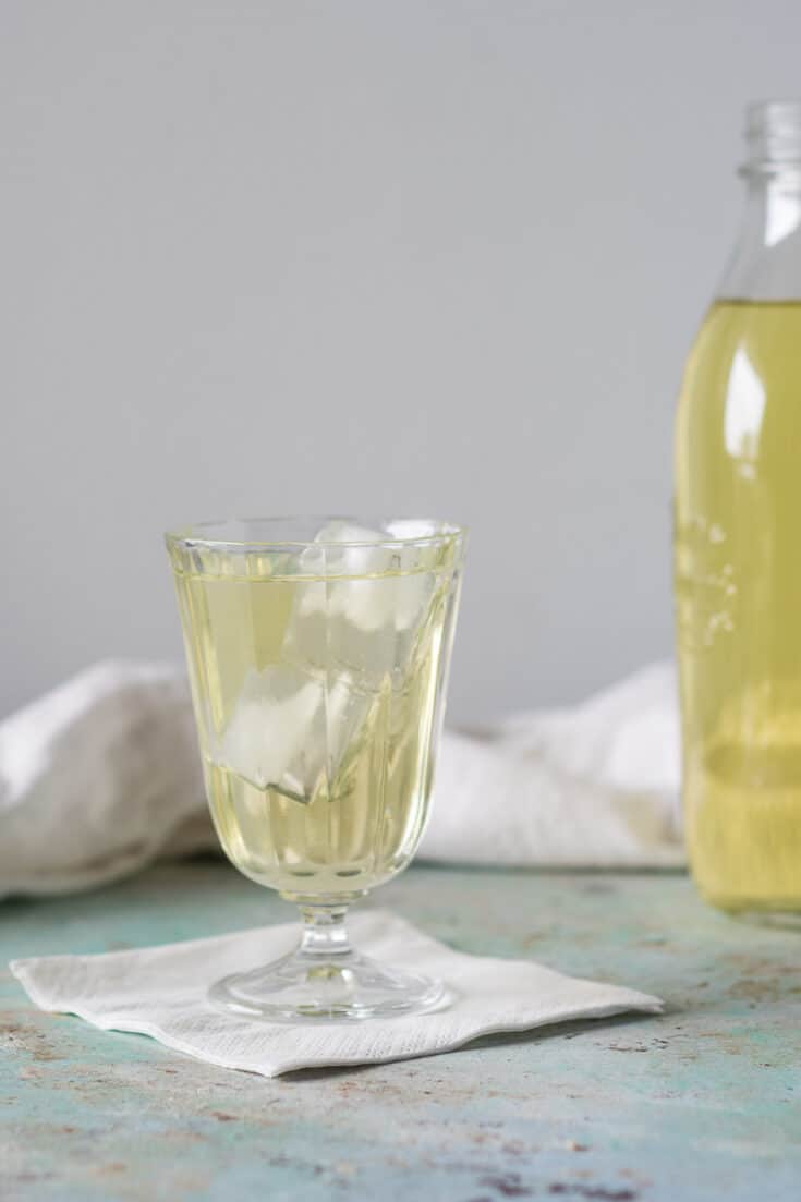 Clarified English Milk Punch in a glass with ice with a bottle of punch in the background