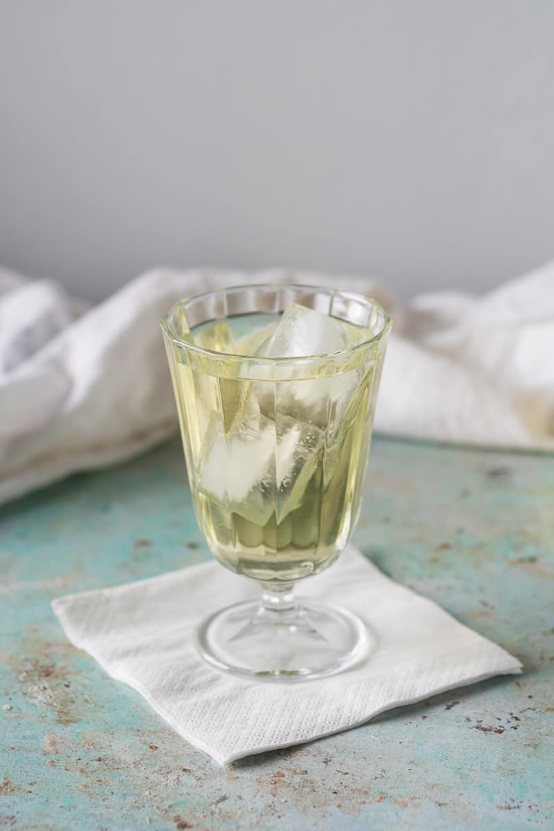 Clarified English Milk Punch in a glass with ice, vertical orientation