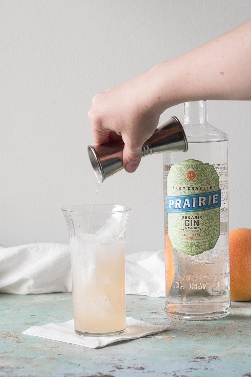 Pouring soda from a jigger into a collins glass