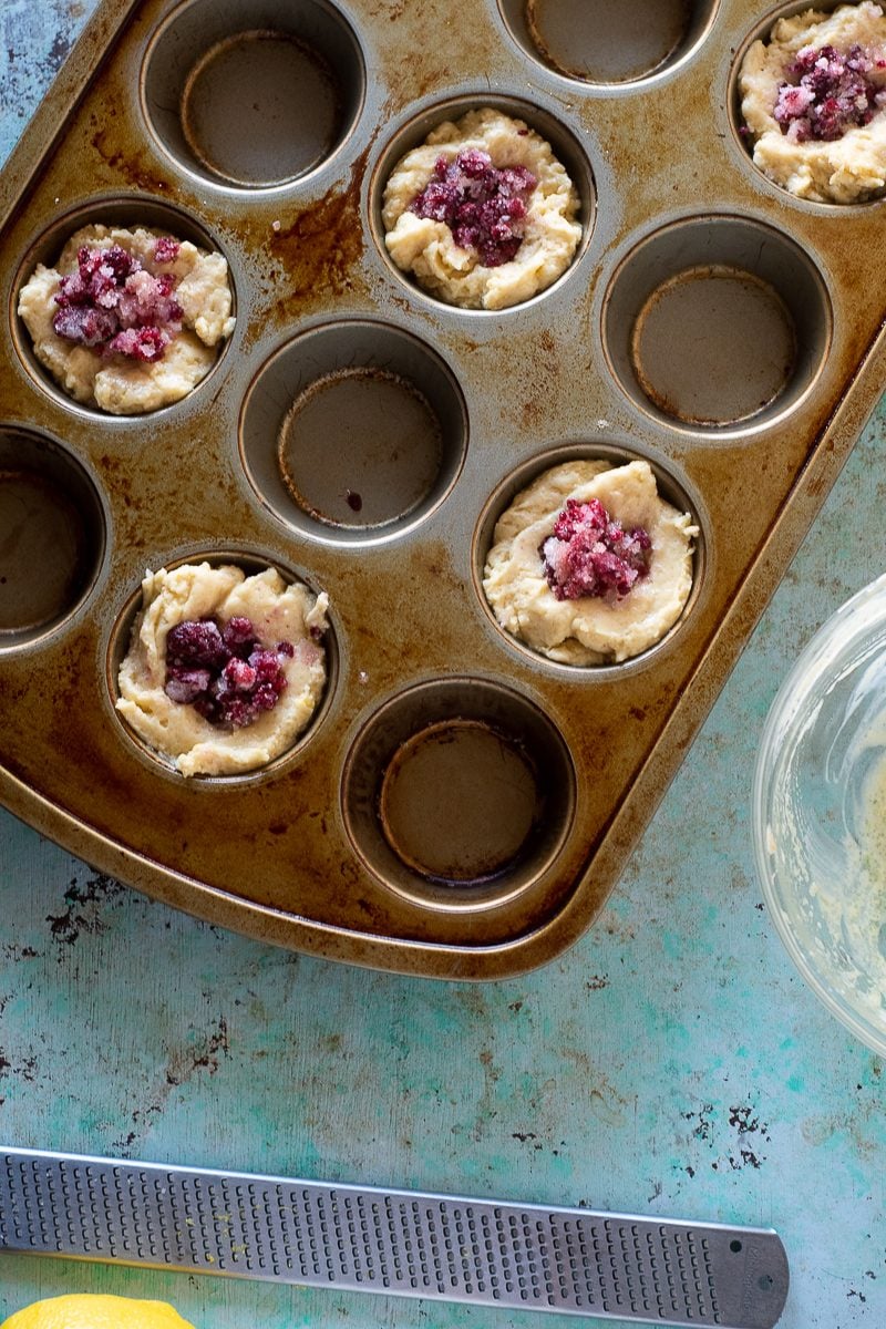Muffin batter with raspberries in a muffin tin
