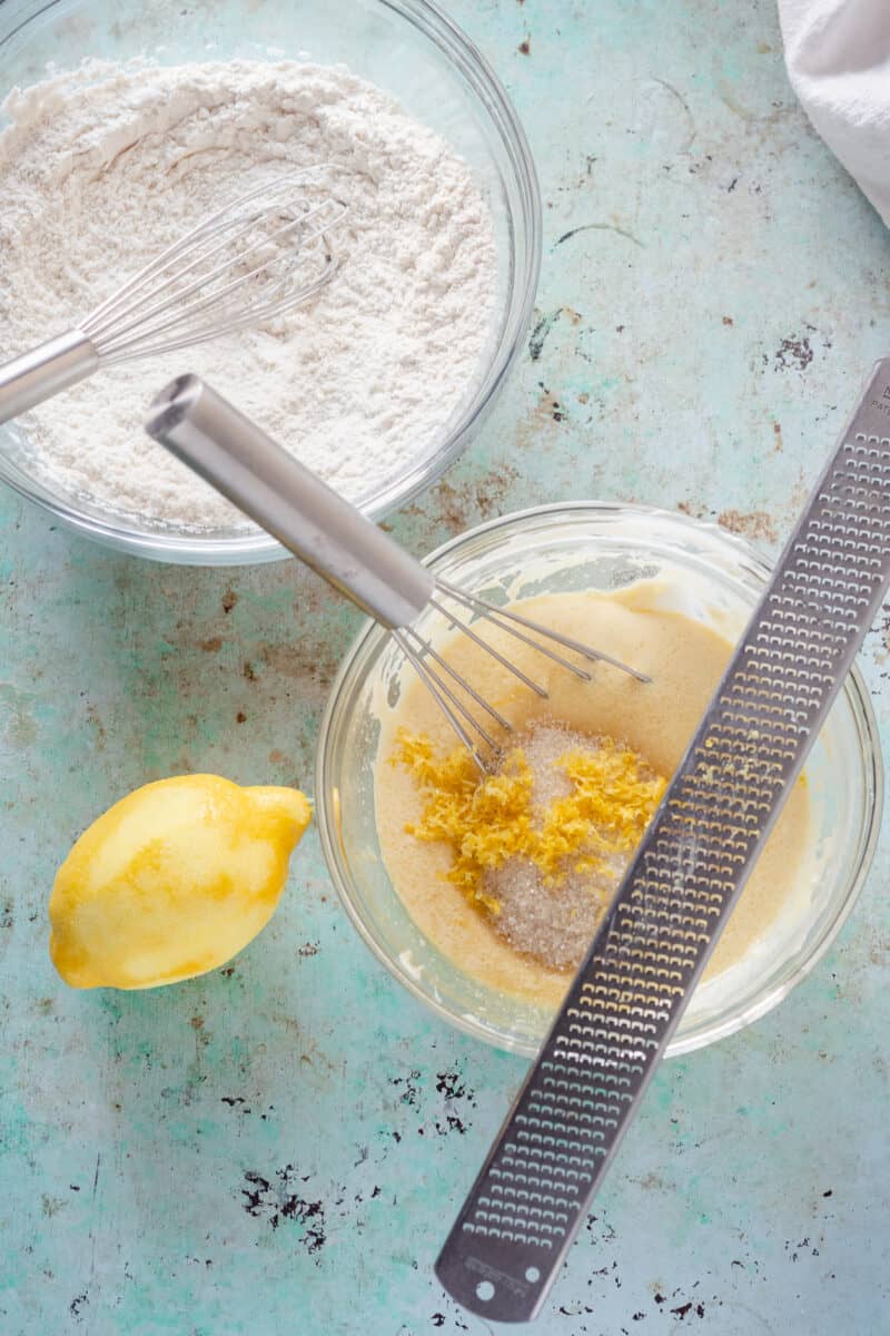 Dry ingredients in a bowl, zested lemon and wet ingredients in another bowl with a zested lemon along side