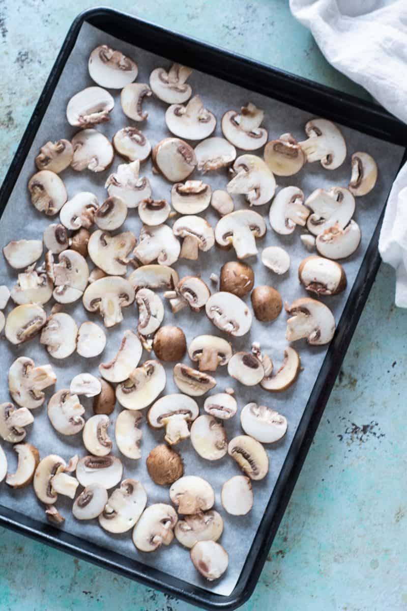 Raw sliced cremini mushrooms on a sheet pan