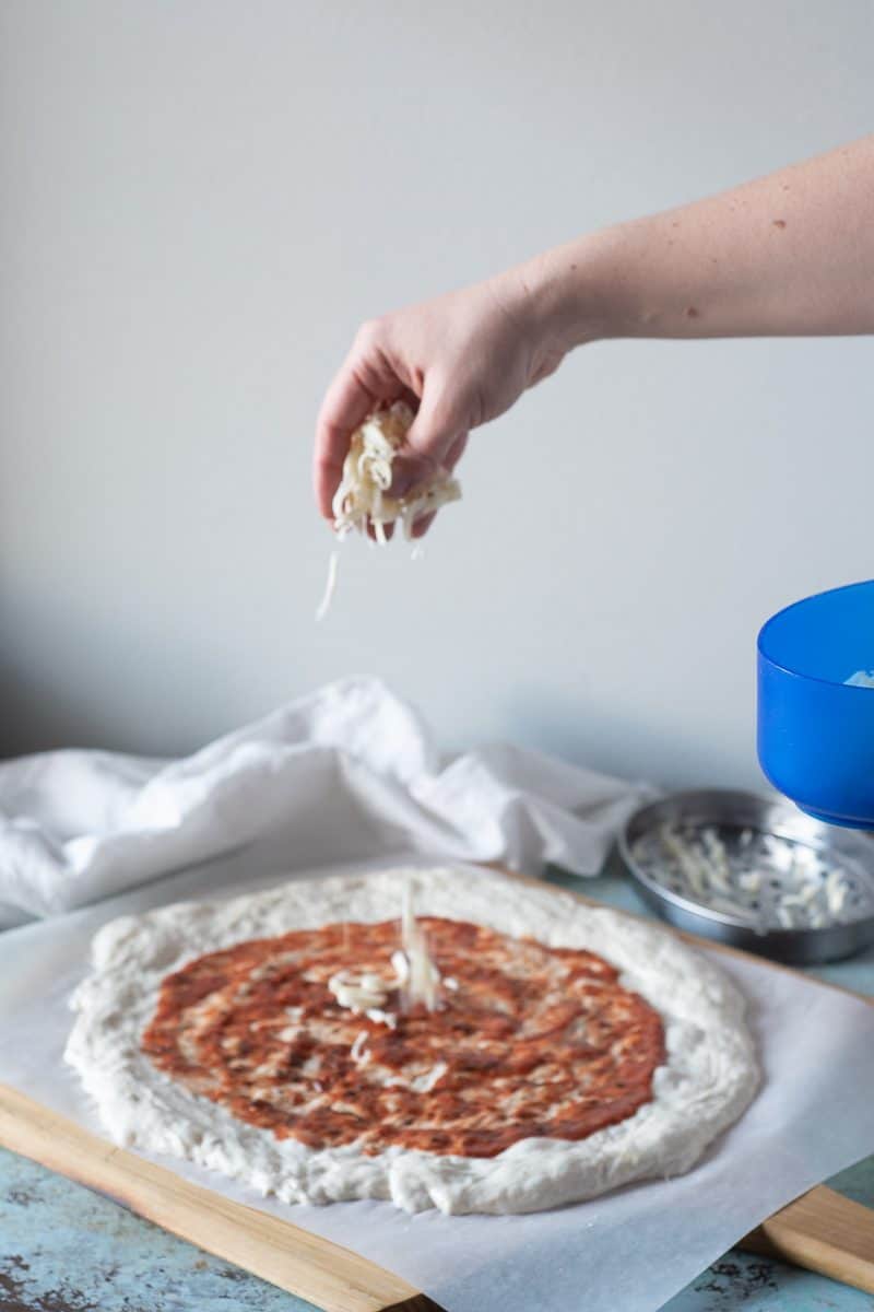 Adding cheese to a sauced round of pizza dough