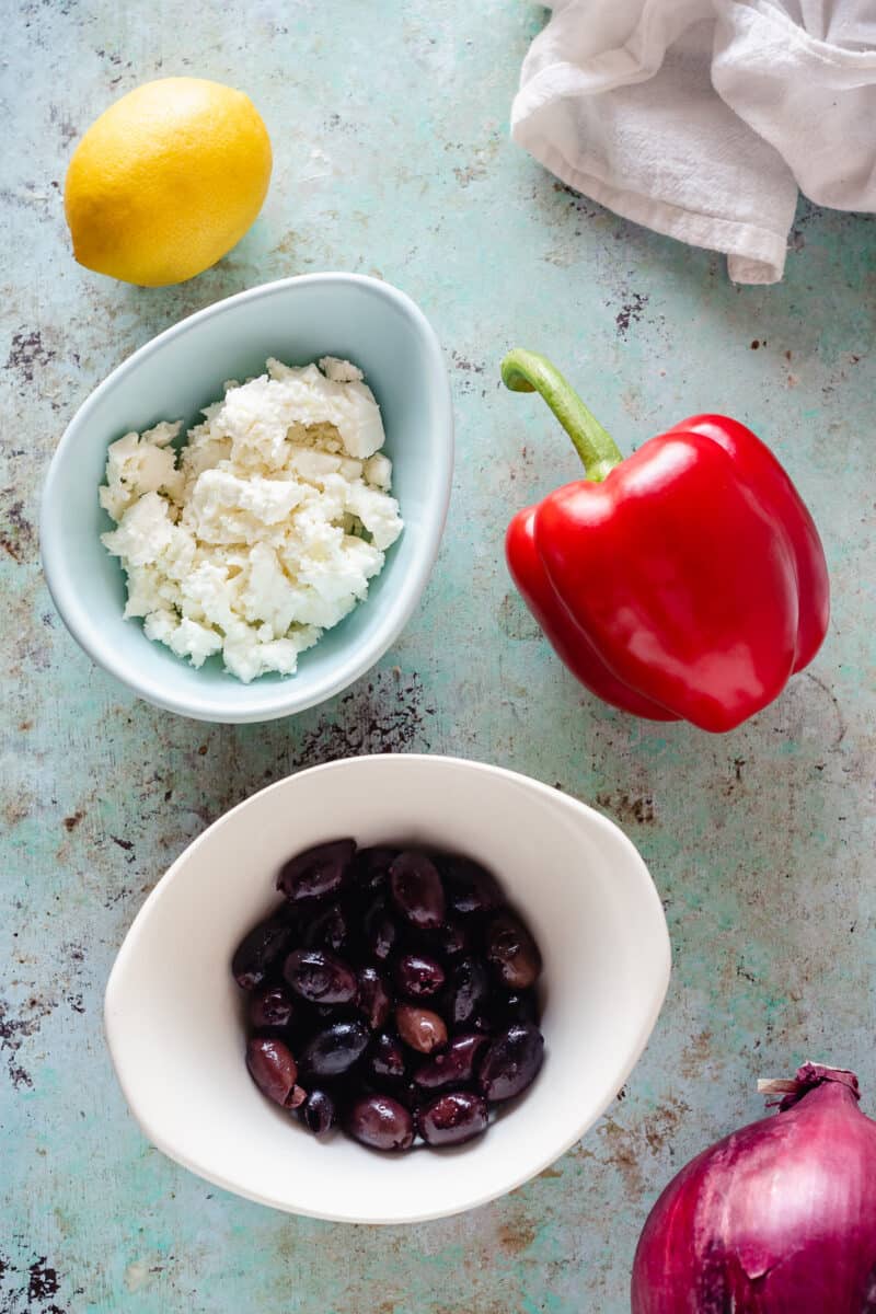 Lemon, feta in a bowl, red bell pepper, and olives on a bowl