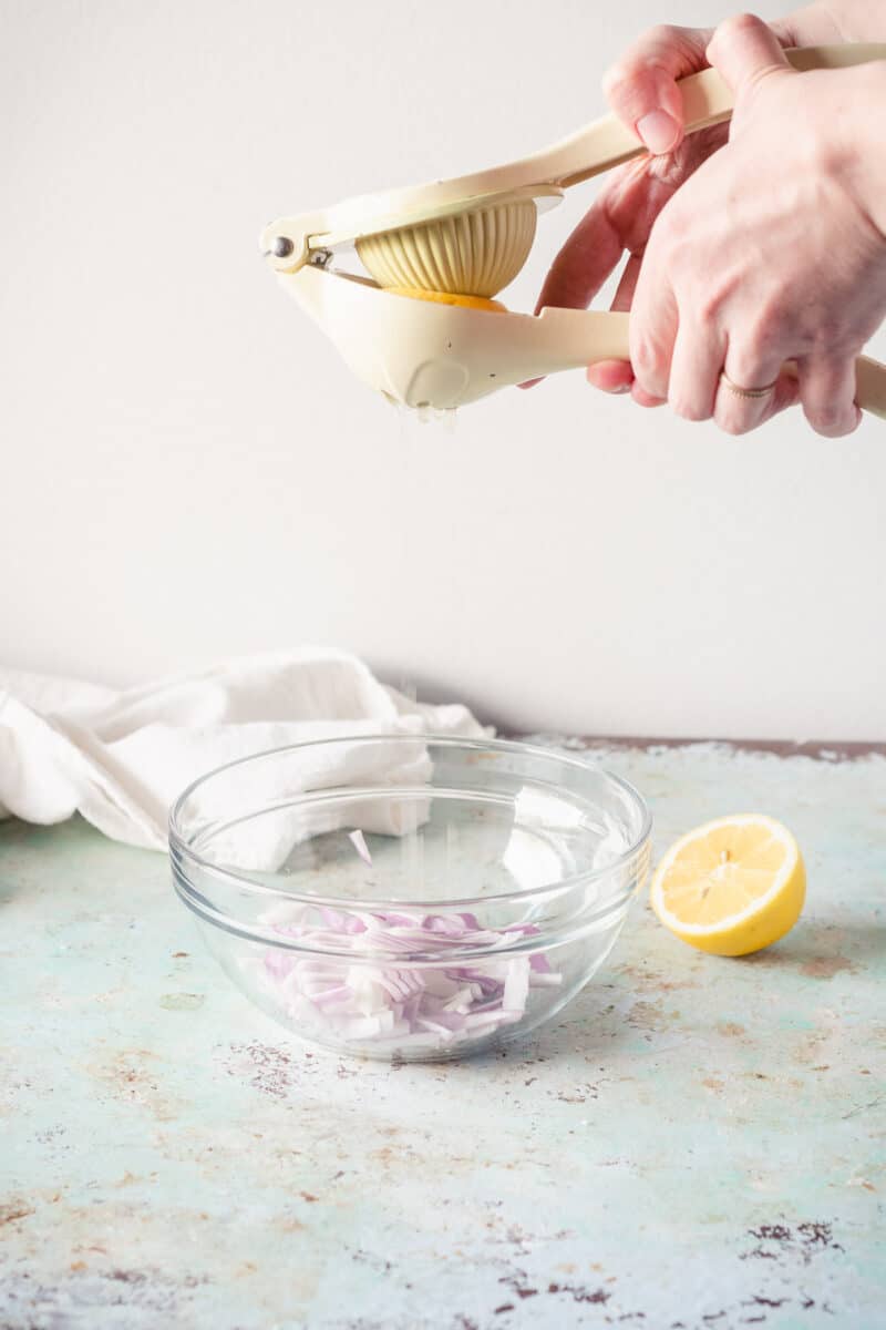 Hands squeezing lemon over sliced red onions