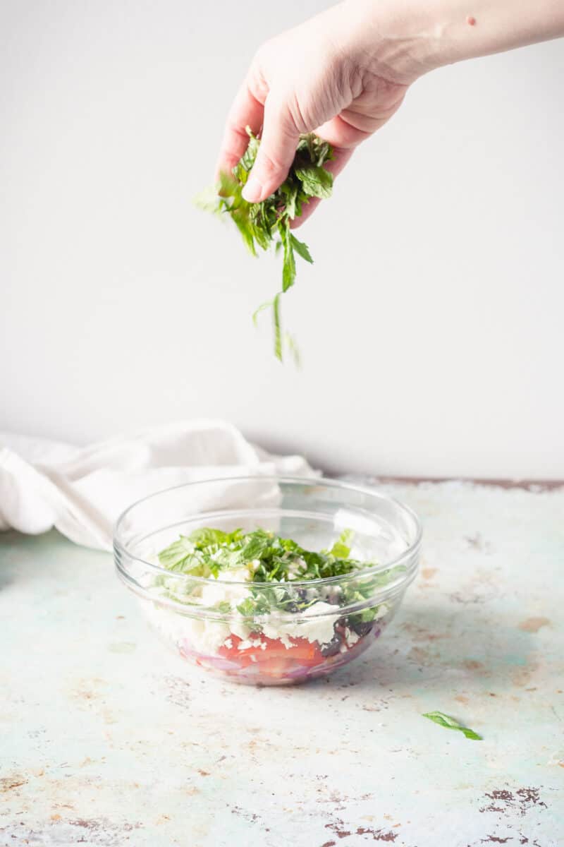 Hand sprinkling mint leaves over marinated feta in a bowl