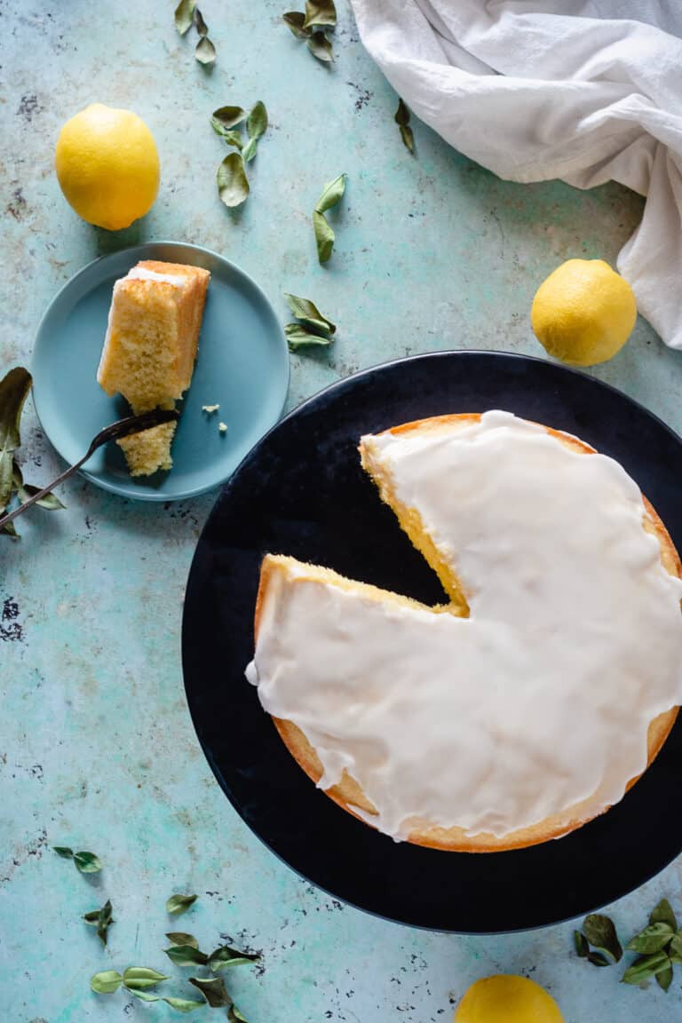 Overhead view of makrut lime leaf cake with lime leaves and lemons scattered around the counter