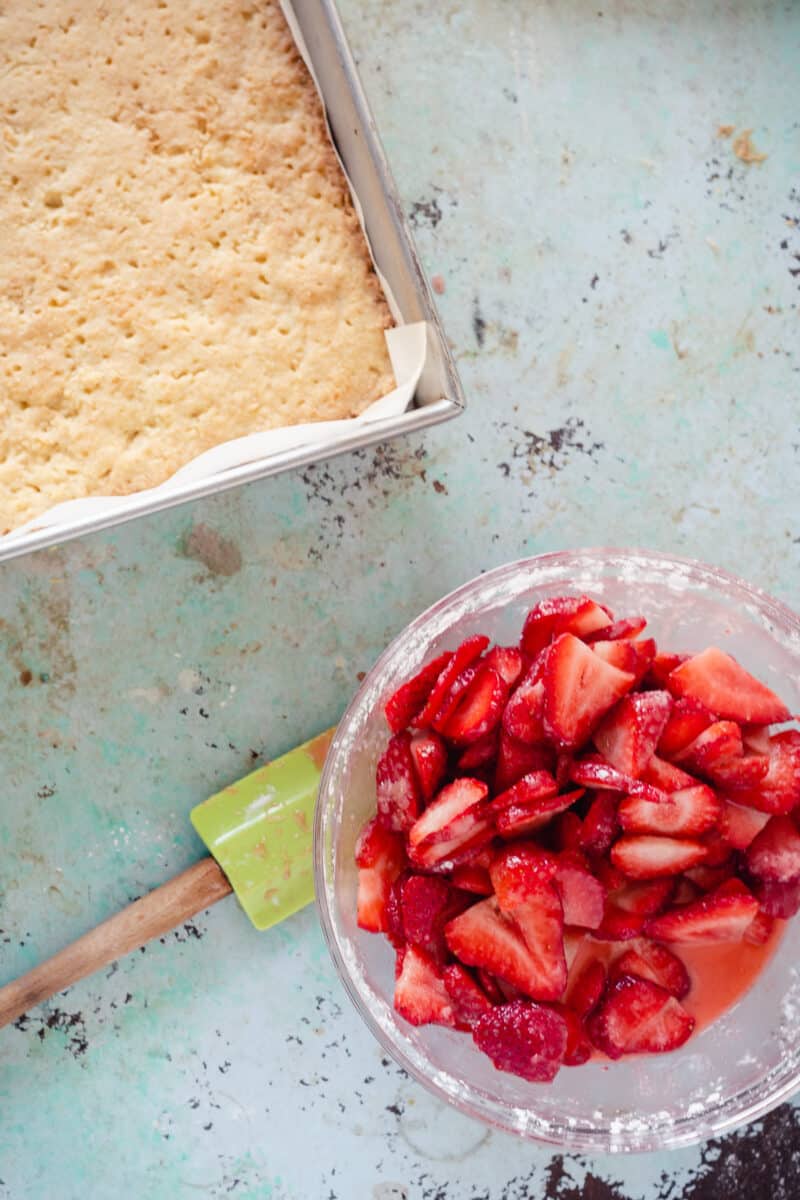 Baked crust in a pan and sliced strawberries in a bowl with sugar