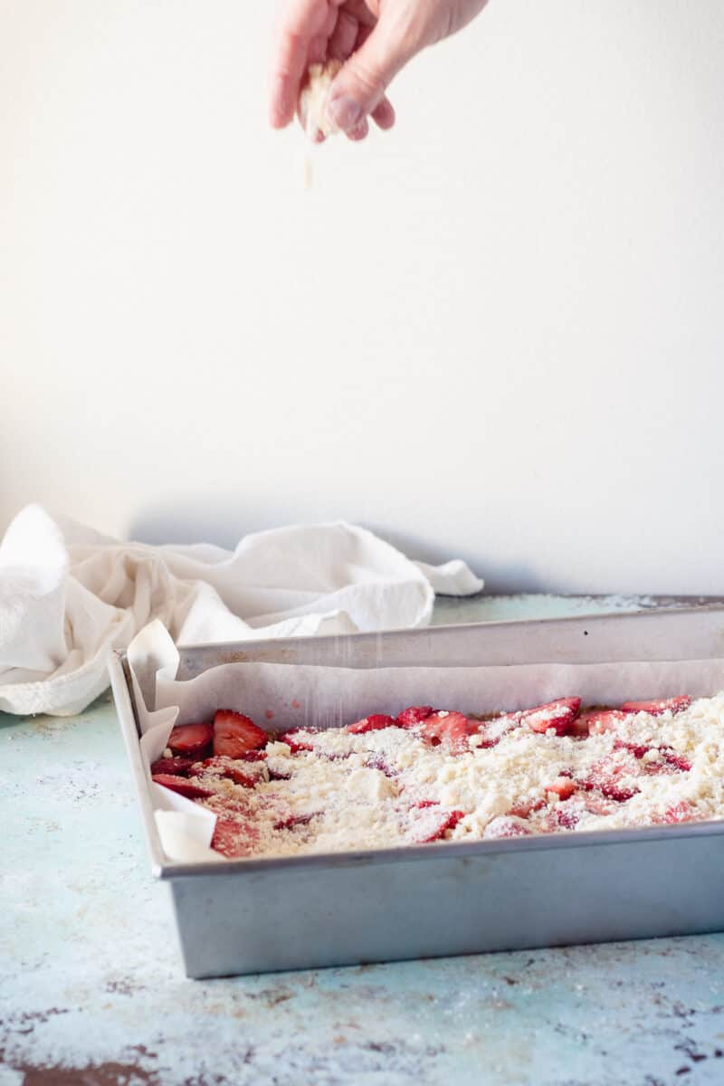 Hand sprinkling crumb topping over strawberry bars