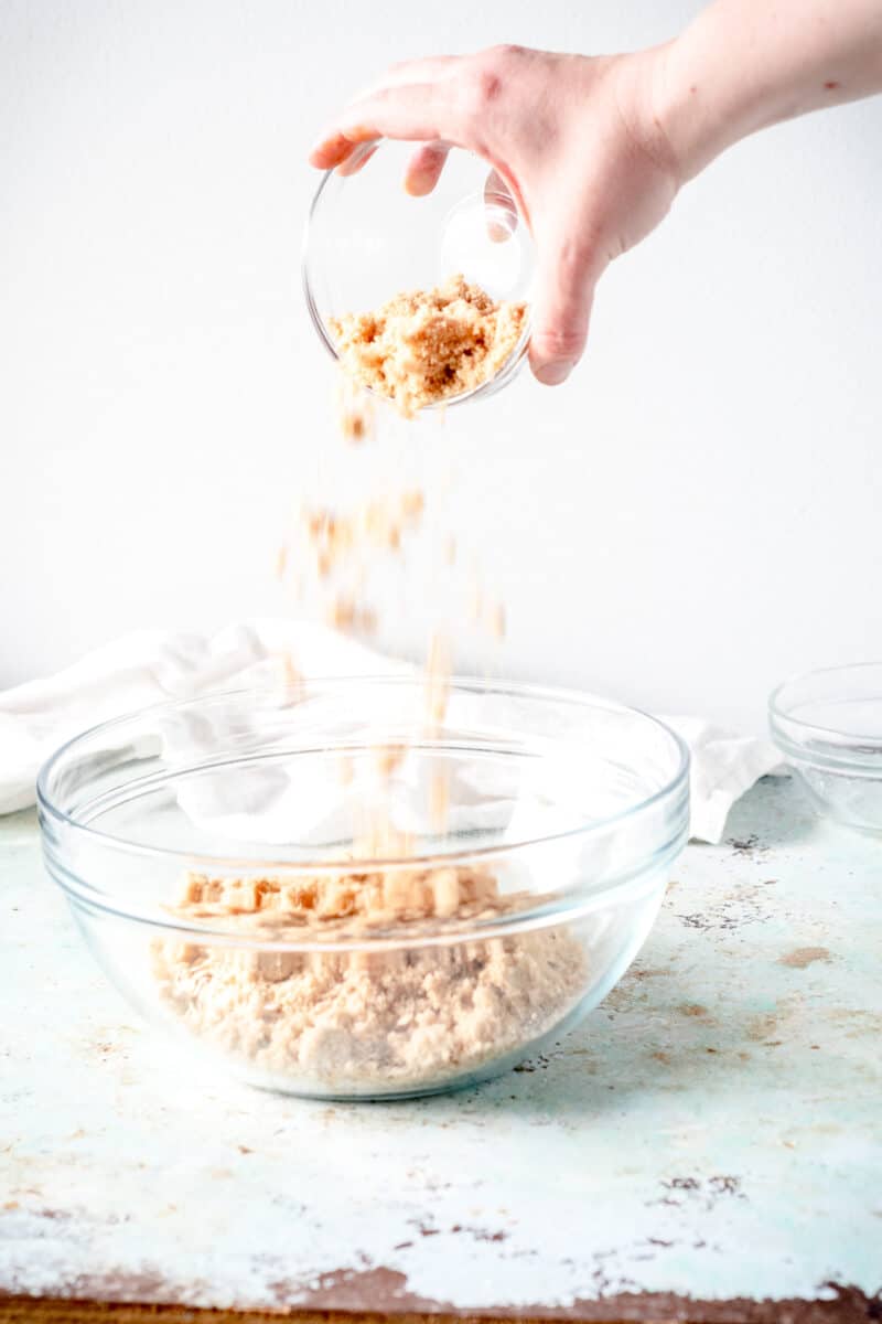 Hand pouring brown sugar into a glass mixing bowl