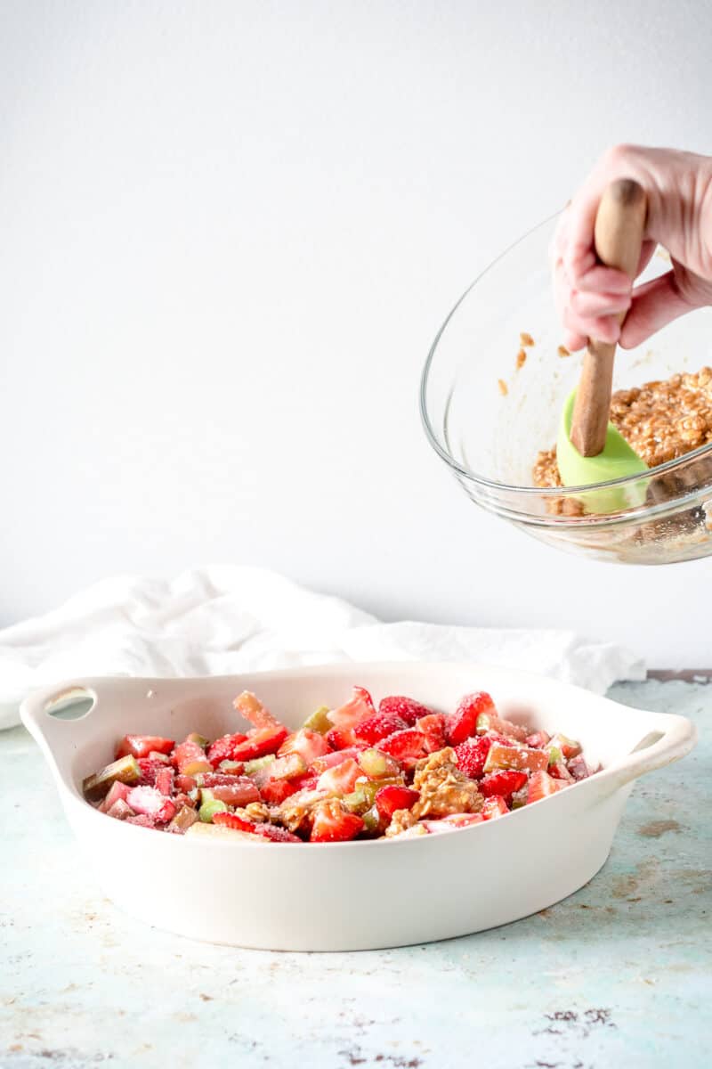 Hand spooning crisp topping over strawberry rhubarb mixture