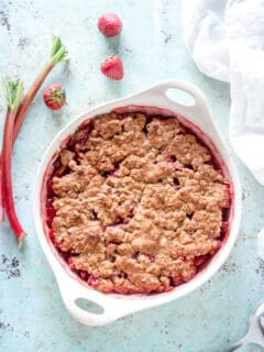 Oat Flour Strawberry Rhubarb Crisp in a baking dish with strawberries and rhubarb stalks nearby