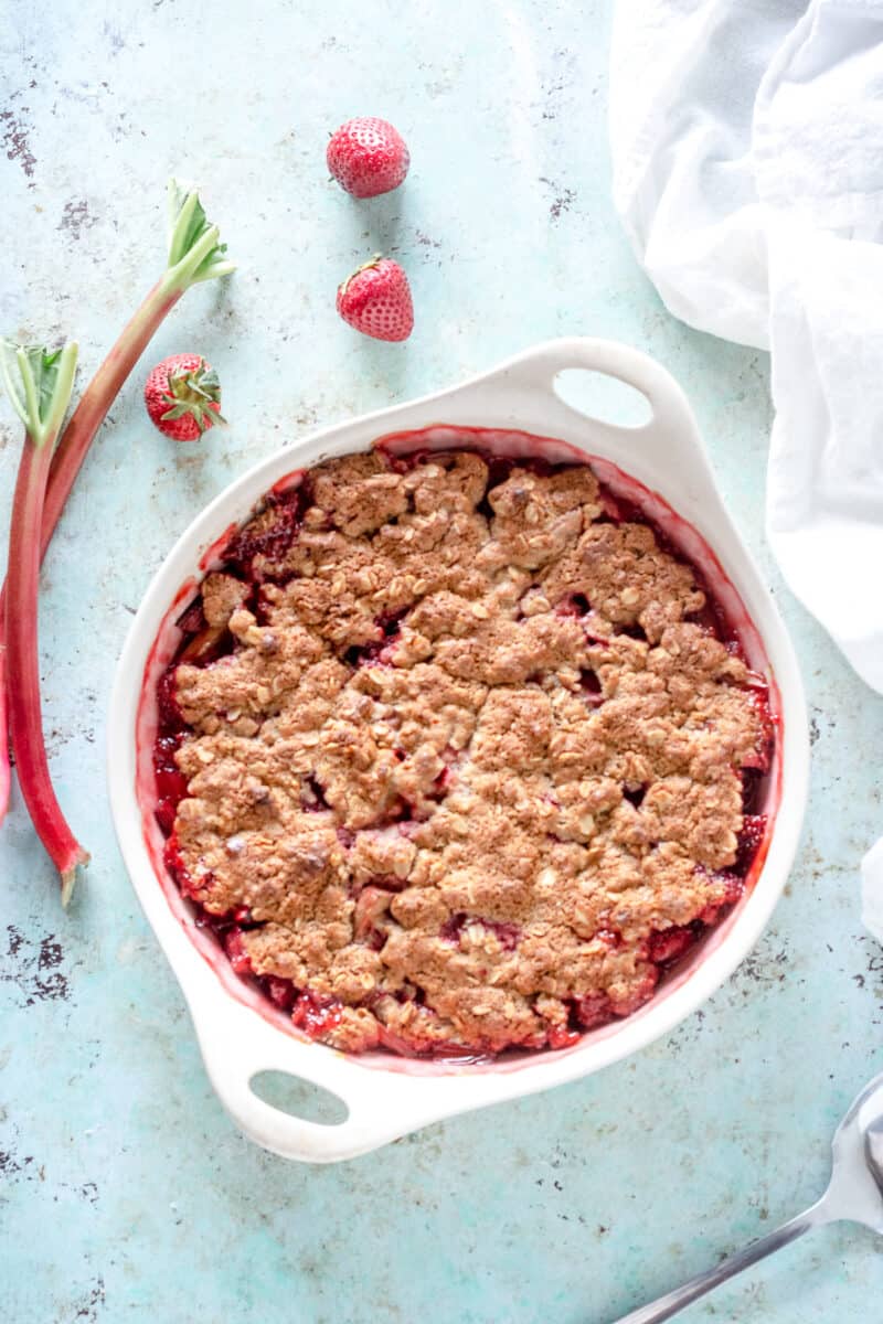 Oat Flour Strawberry Rhubarb Crisp in a baking dish with strawberries and rhubarb stalks nearby