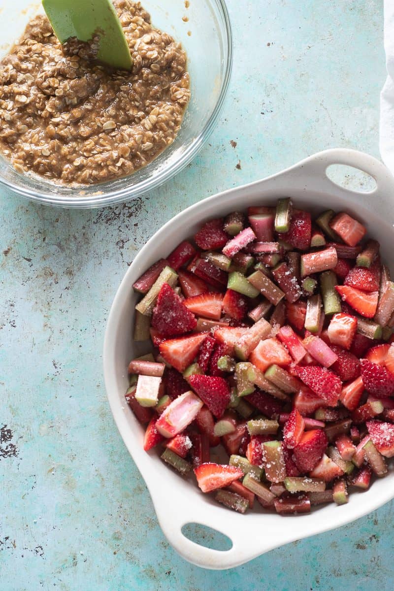 Strawberries and rhubarb in a baking dish with crisp topping in a separate bowl