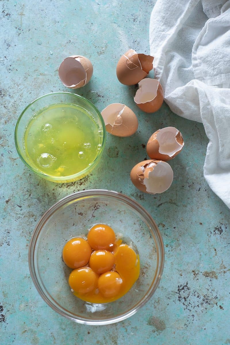Egg white and egg yolks, separated in bowls, with egg shells on the side