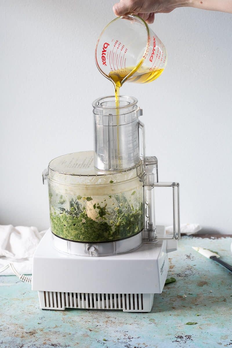 Olive oil being poured over the basil mixture