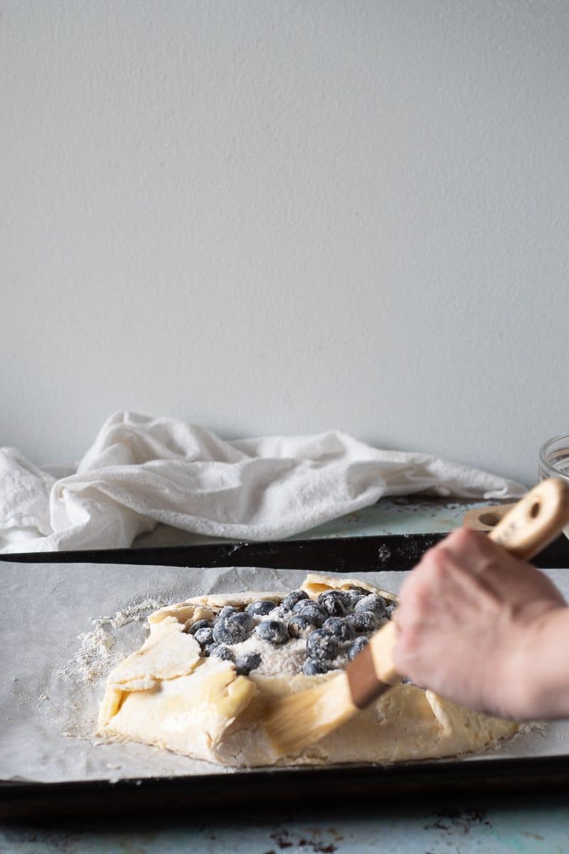 Adding egg wash to blueberry galette