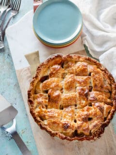 Apple Pie with a lattice top crust on a serving board with a stack of dessert plates next to it