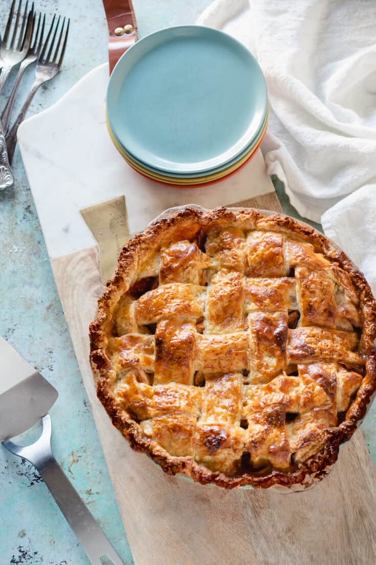 Apple Pie with a lattice top crust on a serving board with a stack of dessert plates next to it