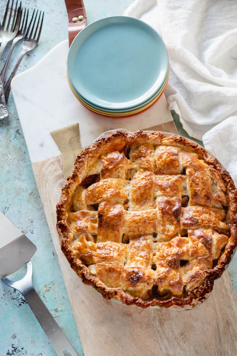 Apple Pie with a lattice top crust on a serving board with a stack of dessert plates next to it