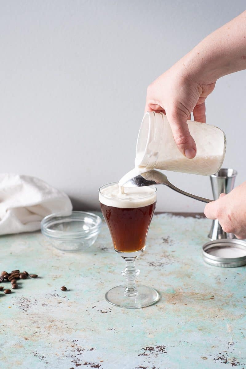 Pouring gently whipped cream over the back of a spoon to top an Irish coffee