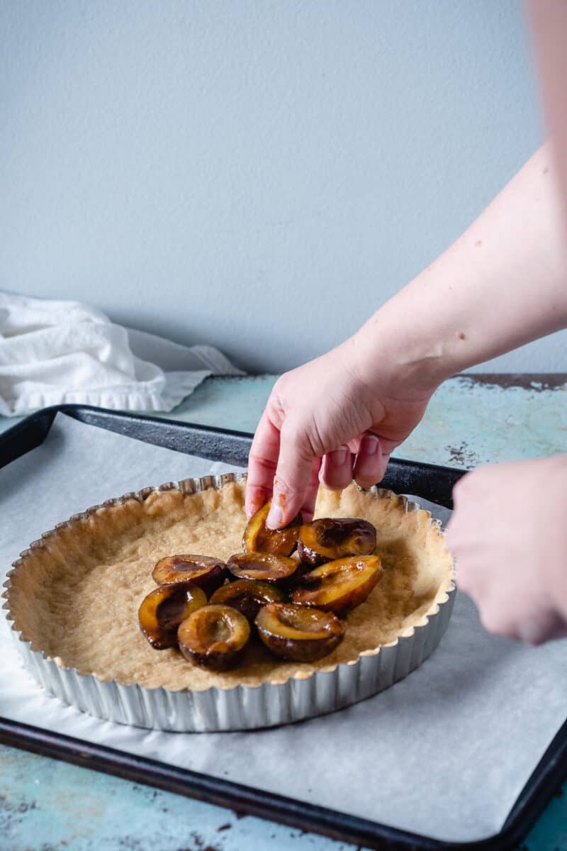 Hand putting plums on a tart crust