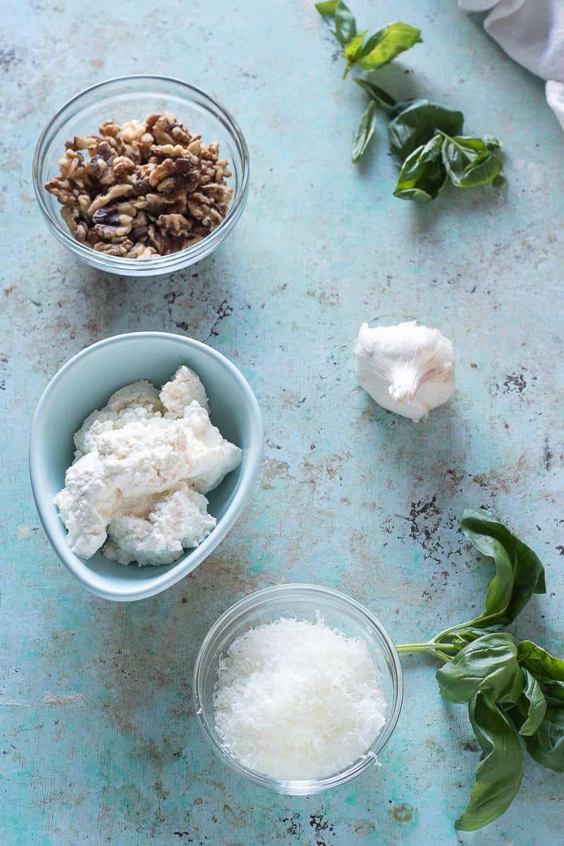 Walnuts, garlic, pecorino romano, and fresh ricotta cheese, and sprigs of basil in bowls