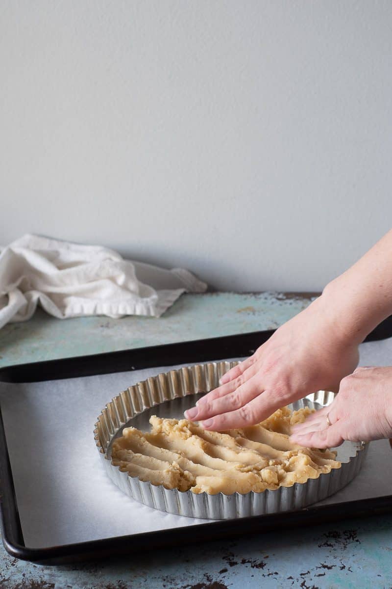 Shortbread tart crust being pressed into a tart pan