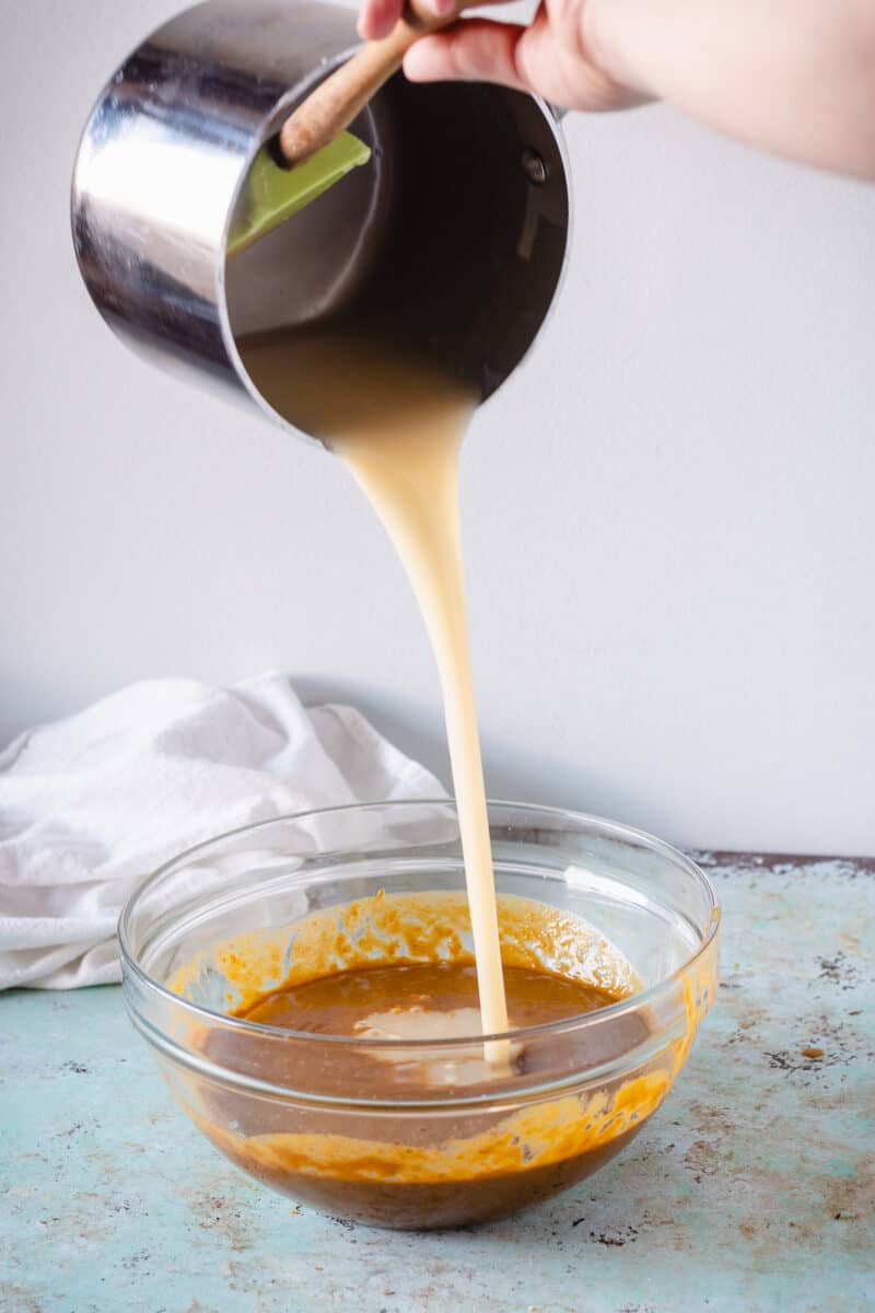 Caramel poured from a saucepan into a mixing bowl with pumpkin mixture